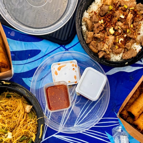Overhead view of takeout containers with spring rolls, noodles, beef and rice, and sauces.