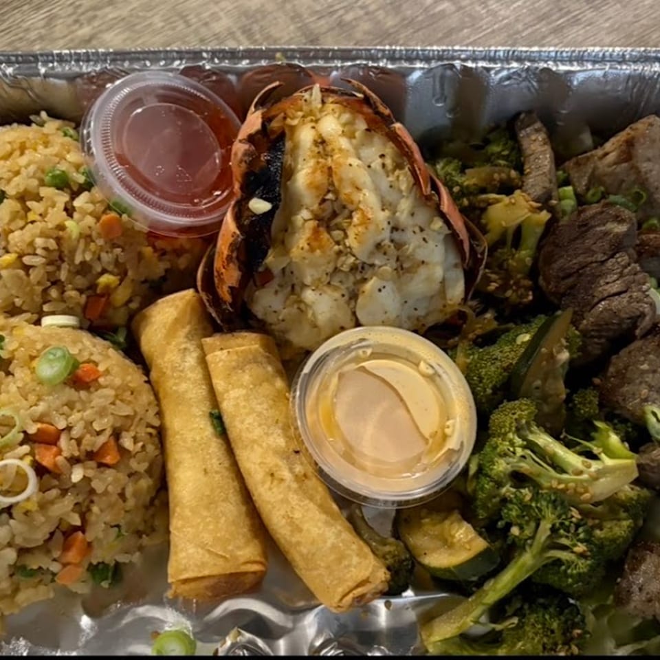 A takeout container with fried rice, lobster tail, egg rolls, beef, and broccoli.