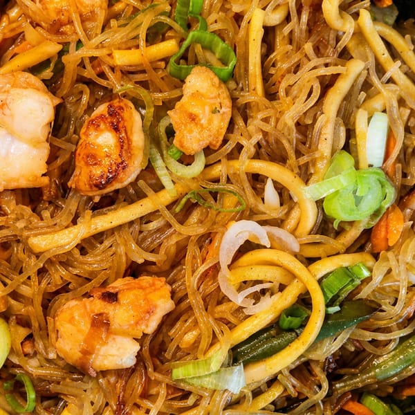 Close-up of shrimp and noodles with vegetables in a black bowl.