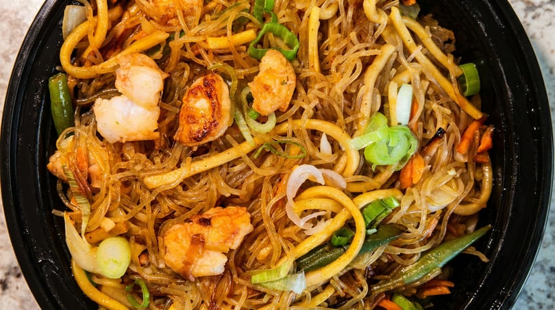 Close-up of shrimp and noodles with vegetables in a black bowl.