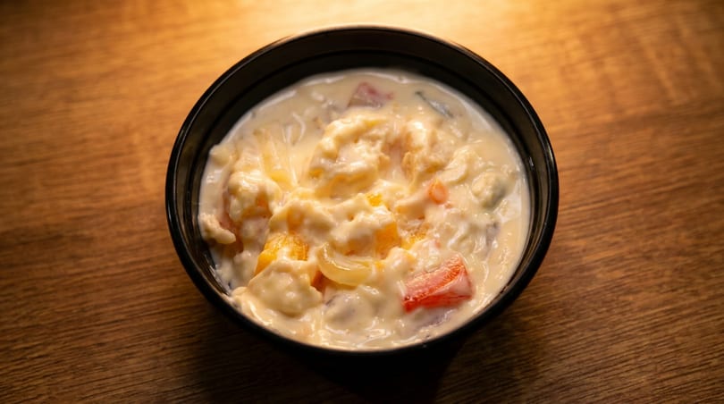 A black bowl filled with creamy fruit salad, featuring peaches, pineapple, and red fruit pieces.